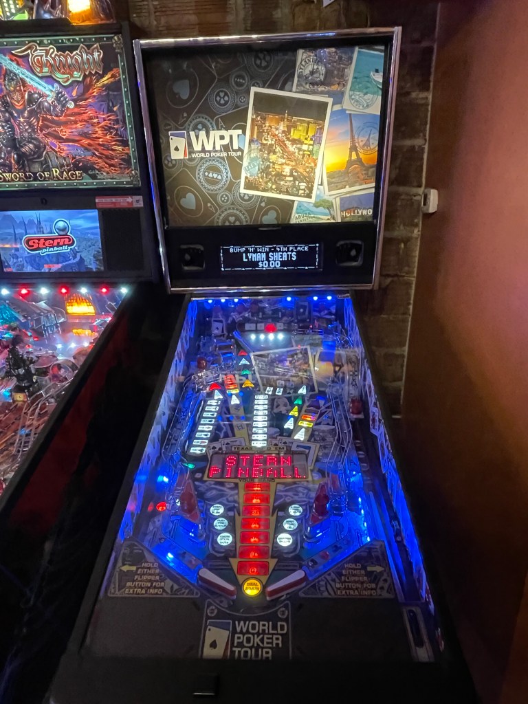 Close-up view of the 'World Poker Tour' pinball machine at Cherry Lanes Arcade Bar, featuring illuminated buttons, playing field, and themed graphics.